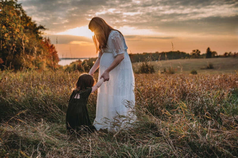 pregnant mother holding her daughter's hands in a field at sunset