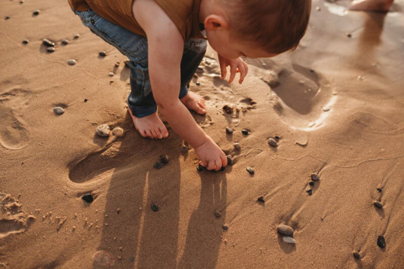 Young boy picking up rocks on a beach during an oshawa family photography session. 