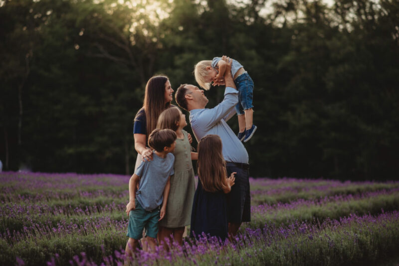 Family of five standing in a field of lavender at Laveanne Lavender farm, dad lifts the youngest boy over his head.