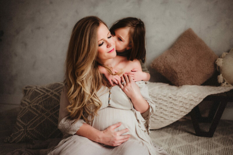 Pregnant mother holding her belly while her young daughter hugs her in s a studio in Oshawa