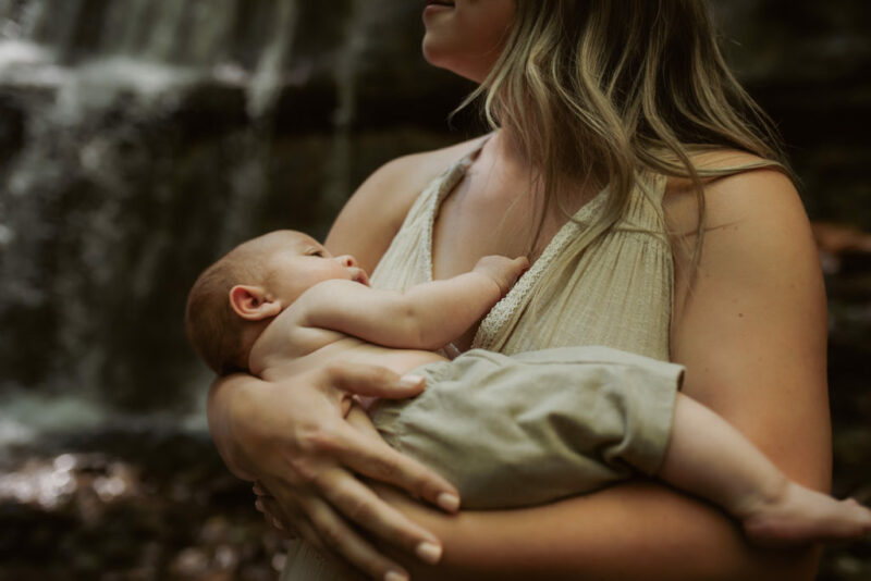 Close up of a newborn in his mother's arms during a newborn photography session by a waterfall