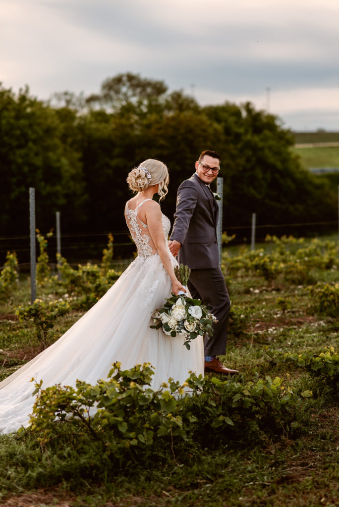 Groom leading a bride through a vineyard field at sunset