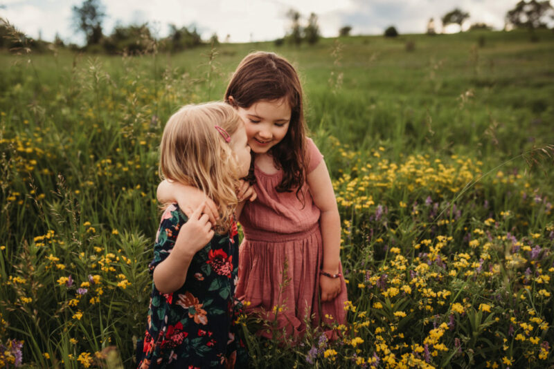 Two young girls hugging in a field of wildflowers