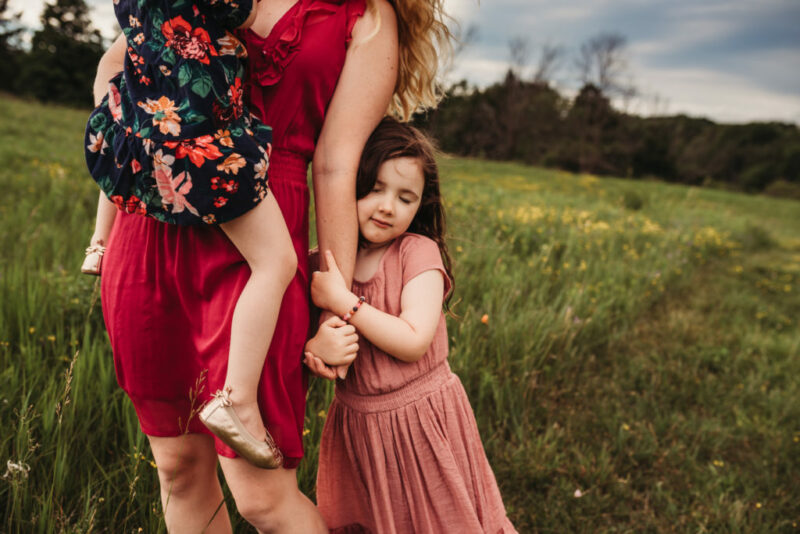 Daughter closing her eyes while hugging her mother's arm in a field at Country Cut Flowers