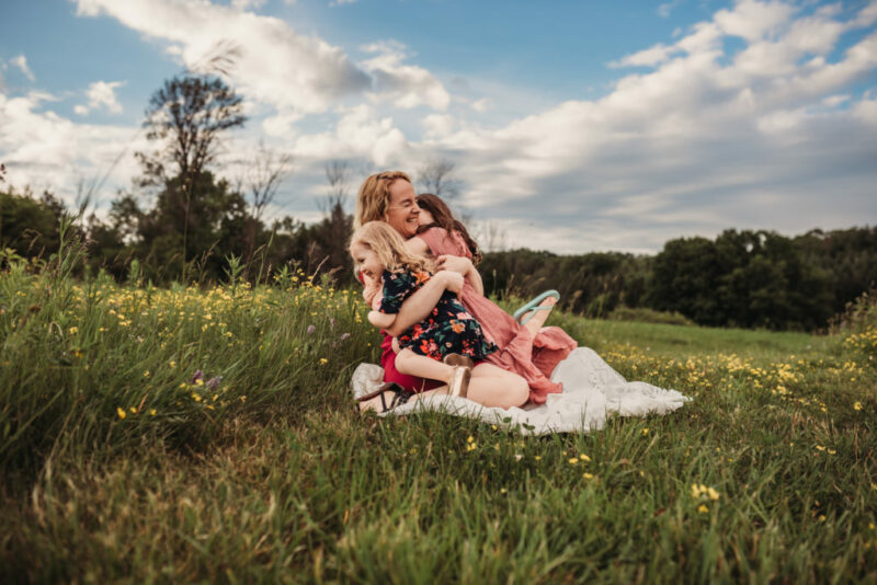 Mother sitting in a field of wildflowers hugging her two daughters at Country Cut Flowers