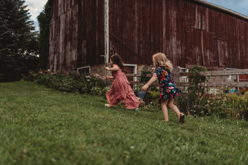 Two young girls running in front of a barn during a photography session at Country Cut flowers