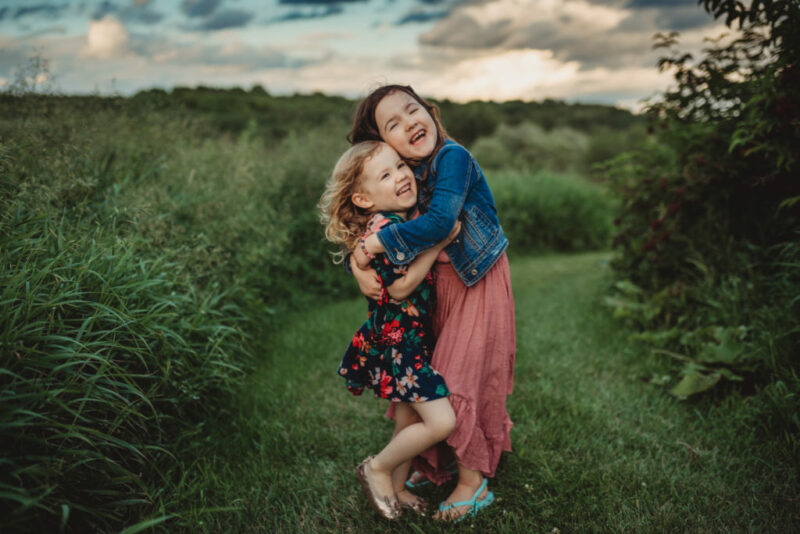 Two young sisters hugging in a field at sunset. 