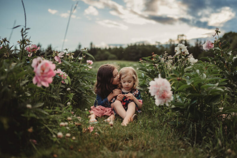 Two sisters telling secrets in a field of peonies during a family photography session at Country Cut Flowers